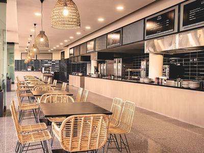 Moderne café-inrichting met rieten stoelen en hangende lampen langs een toonbank.