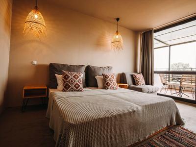 Gezellige hotelkamer met tweepersoonsbed, twee nachtlampjes en balkon met uitzicht buiten.