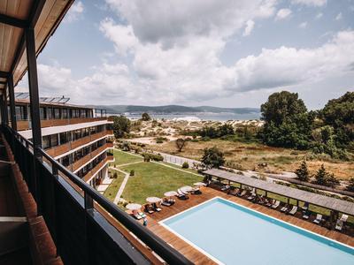Uitzicht op een buitenzwembad en hotelcomplex met bergen en bewolkte lucht op de achtergrond.