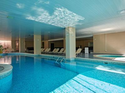 Licht overdekt zwembad met ligstoelen en zuilen in een ontspannen hotelomgeving.