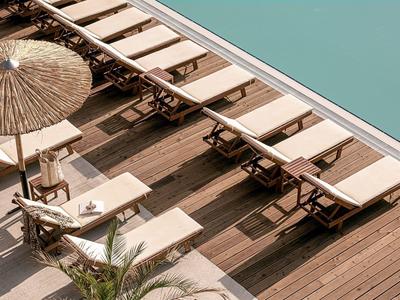 Meerdere ligstoelen langs een zwembad op een houten terras met een parasol.
