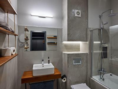 Moderne badkamer met wastafel, spiegel, bad met glazen afscheiding en lichte muren.