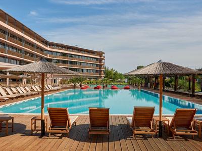 Piscina di un hotel moderno con lettini e ombrelloni su un ponte di legno sotto un cielo azzurro.