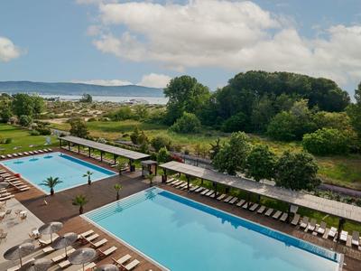 Buitenzwembaden met ligstoelen bij een hotel naast groen landschap en uitzicht op afstand.