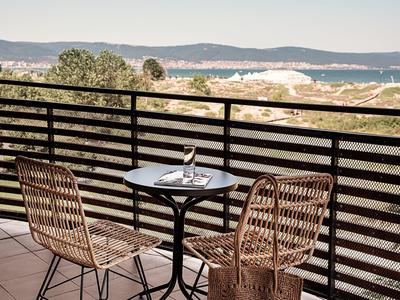 Balkon met twee stoelen en een klein tafeltje met uitzicht op beboste heuvels en zee.