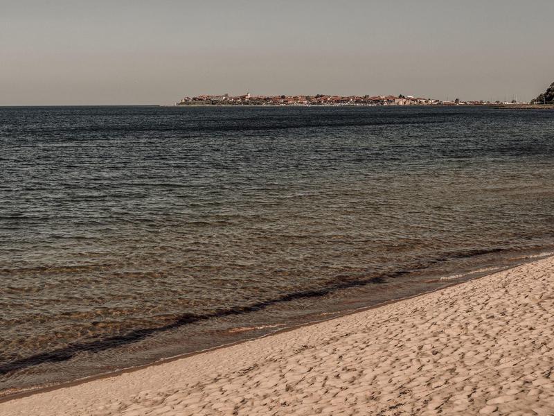 Klarig zandstrand met rustige zee en een verre landtong aan de horizon.