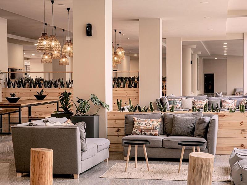 Moderne hotelkamer met gezellige grijze banken, houten krukken en planten.