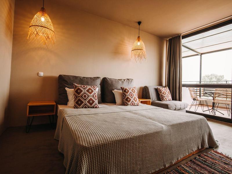 Gezellige hotelkamer met tweepersoonsbed, twee nachtlampjes en balkon met uitzicht buiten.