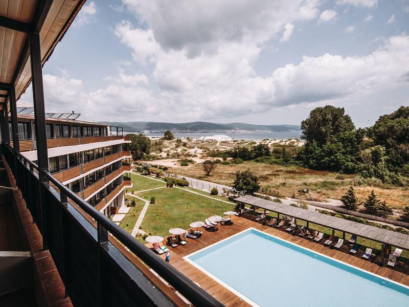 Uitzicht op een buitenzwembad en hotelcomplex met bergen en bewolkte lucht op de achtergrond.
