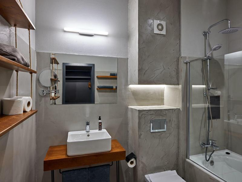 Moderne badkamer met wastafel, spiegel, bad met glazen afscheiding en lichte muren.