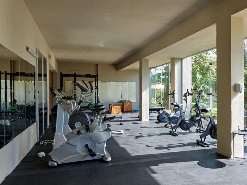 Moderne fitnessruimte met diverse trainingsapparaten en groot raam met uitzicht op groen.