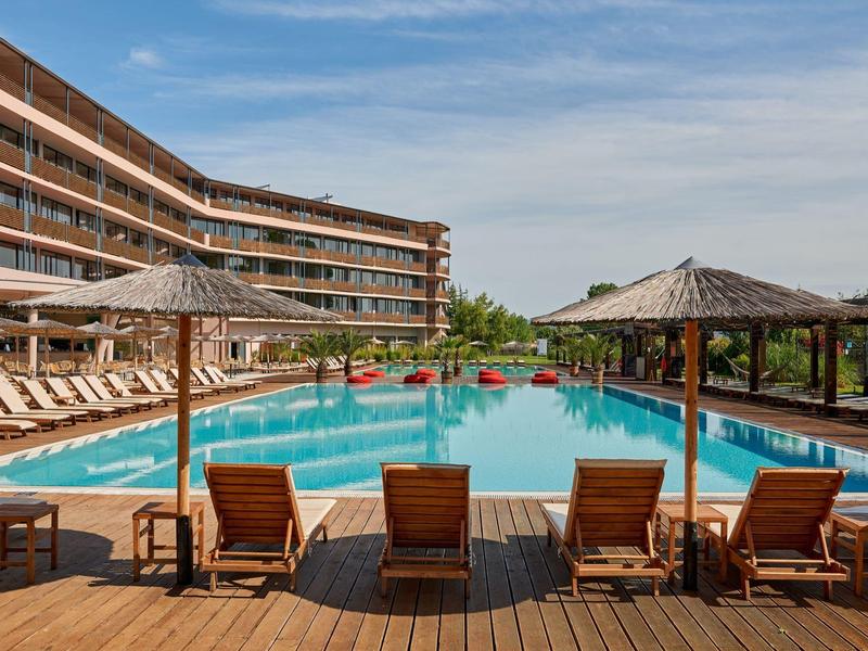 Groot buitenzwembad met ligstoelen en parasols voor een hotelgebouw.