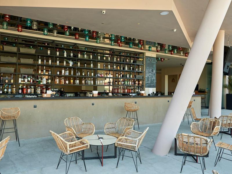 Moderne hotelbar met rotan stoelen en een lange bar met drankjes op de achtergrond.