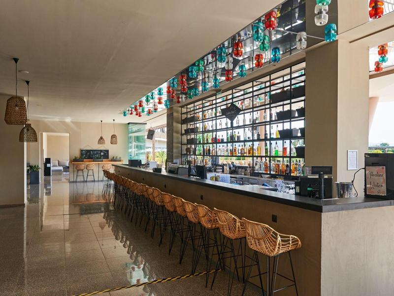 Moderne hotelbar met lange zitplaatsen en kleurrijke decoraties aan het plafond.