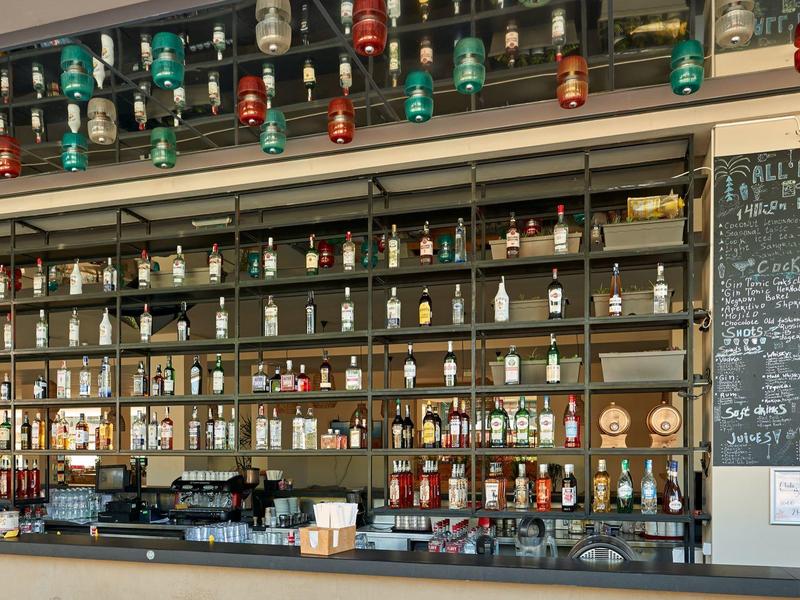 Bar met een grote selectie flessen en kleurrijke glazen lampen aan het plafond.