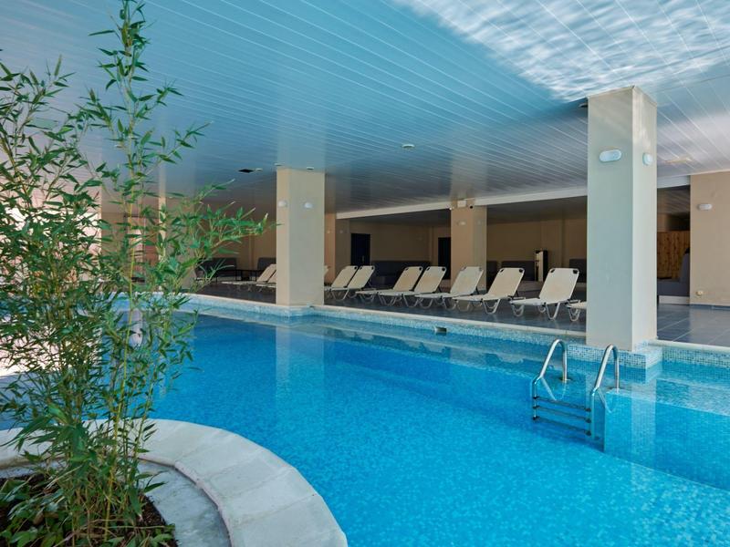 Overdekt zwembad met blauw water, ligstoelen en planten in een luxe hotel.