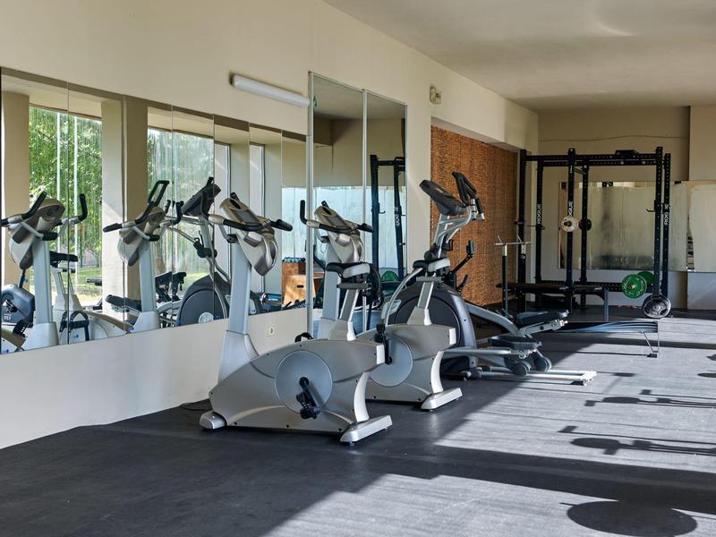 Sportschool met verschillende fitnessapparaten en grote spiegels aan de muur.