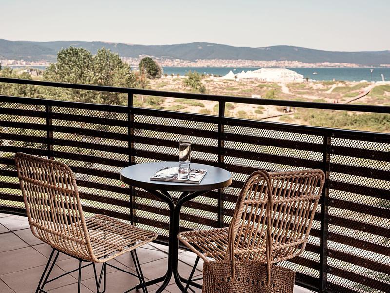 Balkon met twee stoelen en een klein tafeltje met uitzicht op beboste heuvels en zee.