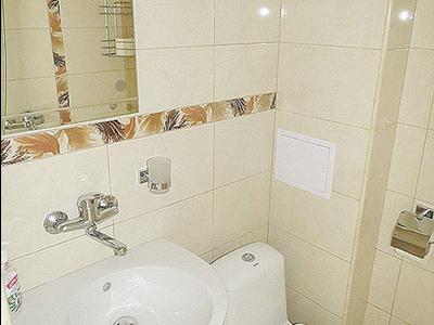 Kleines Badezimmer mit weißer Keramikspüle, WC und beigen Fliesen mit Dekorstreifen.