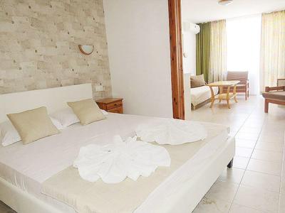 Helles Schlafzimmer mit Doppelbett, weißen und beigen Stoffen, angrenzendem Wohnbereich und großen Fenstern.