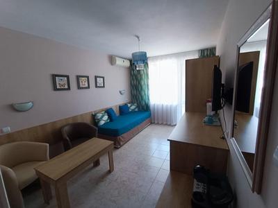 Kleines Hotelzimmer mit Tagesbett, zwei Sesseln, Tisch, Schrank und Fernseher an der Wand.