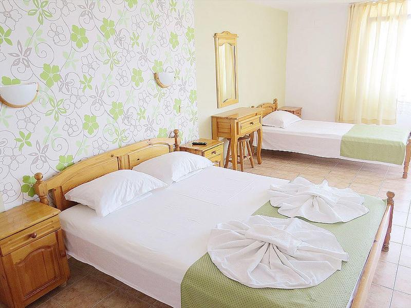 Helles Schlafzimmer mit zwei Holzbetten, grün-weißer Bettwäsche und gemusterter Tapete.