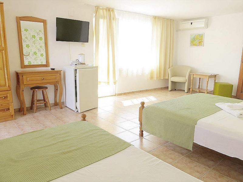 Helles Zimmer mit zwei Einzelbetten, grün-weißer Bettwäsche, Tisch, Fernseher und großem Fenster mit Vorhängen.