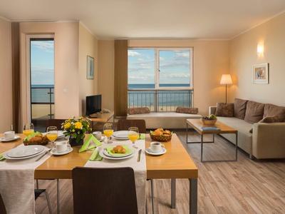 Helles Wohnzimmer mit Esstisch, Sofa, TV, Balkon und Meerblick in warmen Erdtönen.