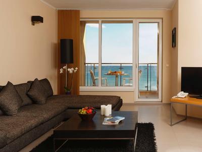 Helles Wohnzimmer mit grauem Sofa, schwarzem Teppich, Holztisch und großer Fensterfront zum Meer.