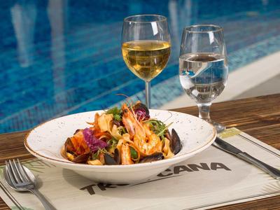 Teller mit Pasta und Garnelen, daneben ein Glas Weißwein und ein Glas Wasser am Pool.