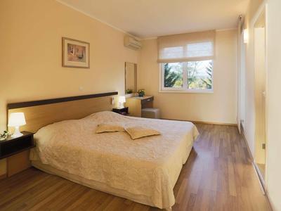 Hell eingerichtetes Schlafzimmer mit großem Bett, Holzboden und einem Fenster mit Sicht ins Grüne.