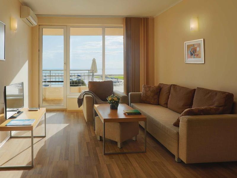 Modernes Wohnzimmer mit braunem Sofa, Holzfußboden, TV und großem Fenster mit Balkonblick.