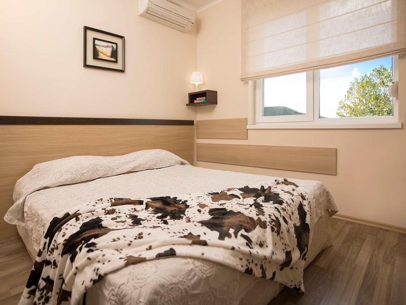 Kleines Schlafzimmer mit Doppelbett, schwarz-weißem Musterplaid, hellen Wänden und Fenster mit Sicht nach draußen.