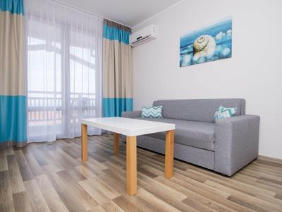 Helles Wohnzimmer mit grauem Sofa, Holztisch, blau-beigen Vorhängen und Bild an weißer Wand.