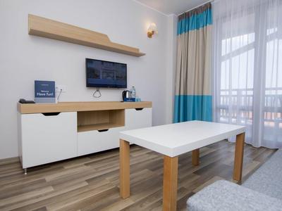 Moderner Wohnraum mit weißem Couchtisch, Sideboard, Wandregal, TV und großem Fenster mit Vorhängen.