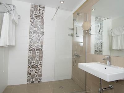 Helles Bad mit weißem Waschbecken, glasduschwand und gemusterten Fliesen in Dusche.