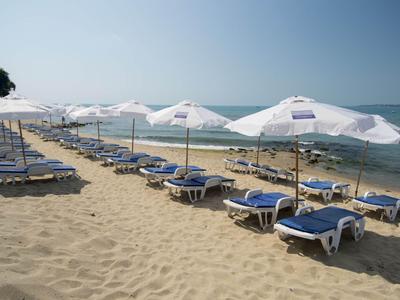 Leere Liegestühle mit weißen Sonnenschirmen am Sandstrand neben ruhigem Meer.