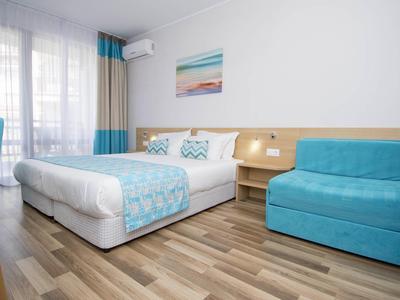 Hell eingerichtetes Schlafzimmer mit Doppelbett, blauem Sessel und Holzboden.