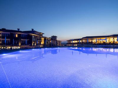 Beleuchteter Poolbereich eines Hotels bei Dämmerung mit modernen Gebäuden im Hintergrund.