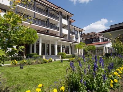Moderne Hotelanlage mit gepflegtem Garten und blühenden Blumen unter blauem Himmel.