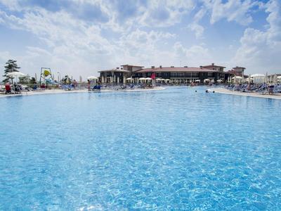 Großes blaues Schwimmbecken unter bewölktem Himmel, umgeben von Menschen und Gebäuden.