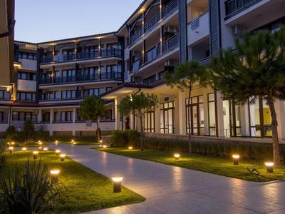 Moderner Hotelhof mit beleuchtetem Weg, kleinen Palmen und umliegenden Balkonen bei Dämmerung.