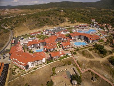 Große Ferienanlage mit vielen Gebäuden, roten Dächern und mehreren blauen Schwimmbädern in hügeliger Landschaft.