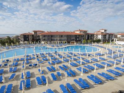 Großer Hotelpool mit vielen blauen Liegestühlen und Sonnenschirmen bei sonnigem Wetter.