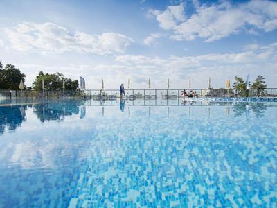 Großer Swimmingpool mit klarem Wasser und blauem Himmel, umgeben von Pflanzen und Stühlen.