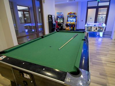 Billardtisch mit Queue in einem hellen Spielraum mit Spielautomaten und Kickertisch.