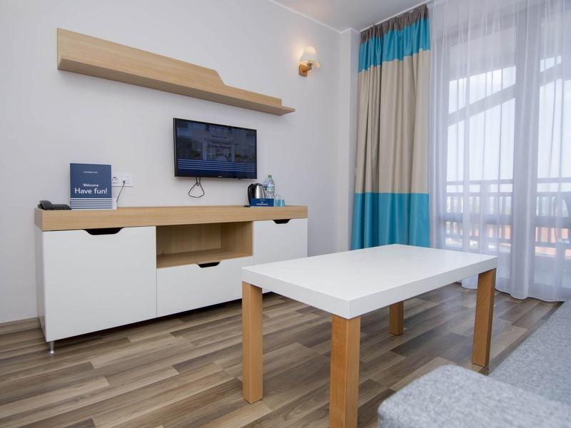 Moderner Wohnraum mit weißem Couchtisch, Sideboard, Wandregal, TV und großem Fenster mit Vorhängen.