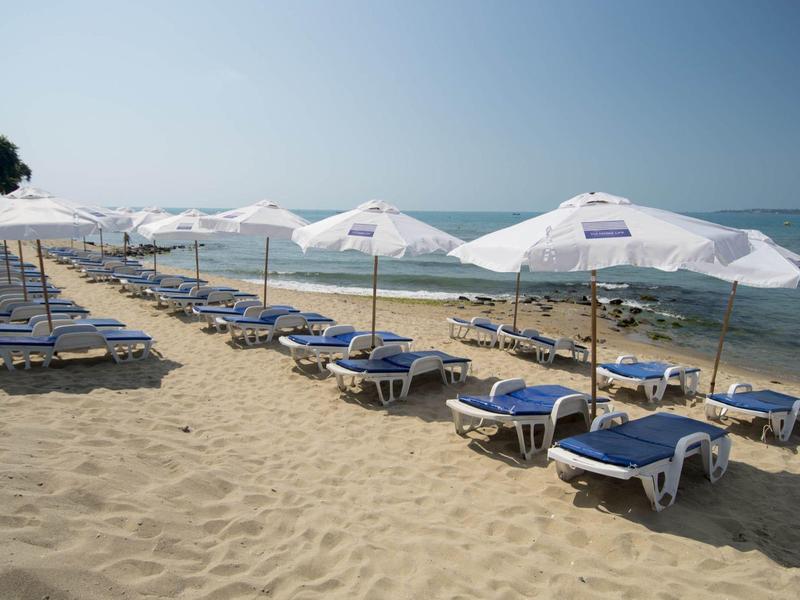 Sandstrand mit vielen weißen Sonnenschirmen und blauen Liegen am ruhigen, blauen Meer.