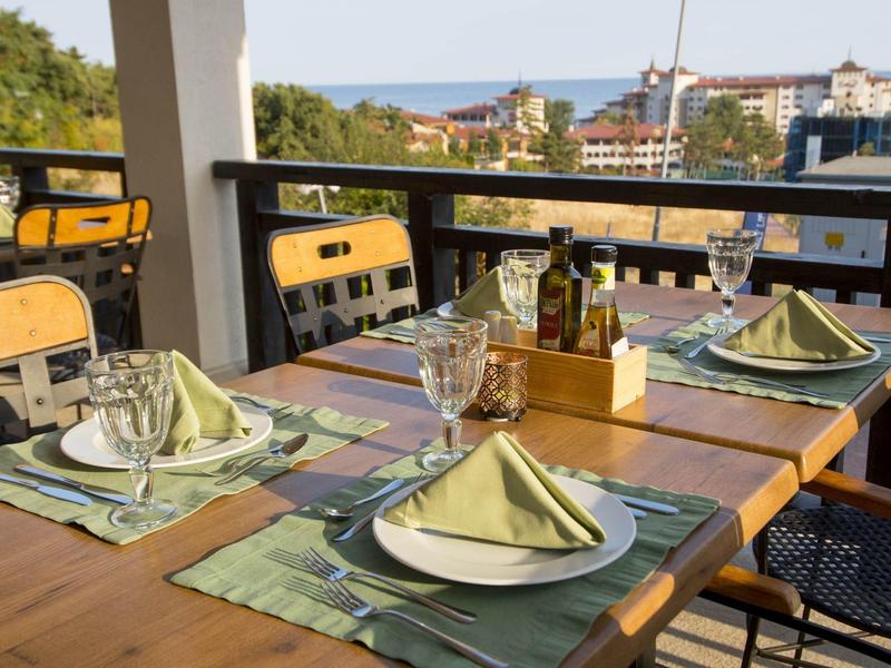 Ein gedeckter Holztisch mit gefalteten Servietten und Glas auf einer Terrasse mit Meerblick.
