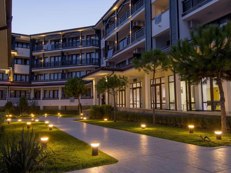 Moderner Hotelhof mit beleuchtetem Weg, kleinen Palmen und umliegenden Balkonen bei Dämmerung.